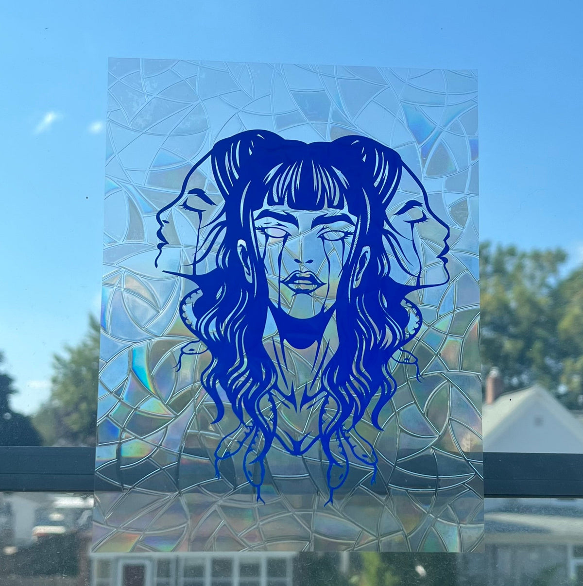 Blue portrait decal on a window with a clear blue sky and houses in the background