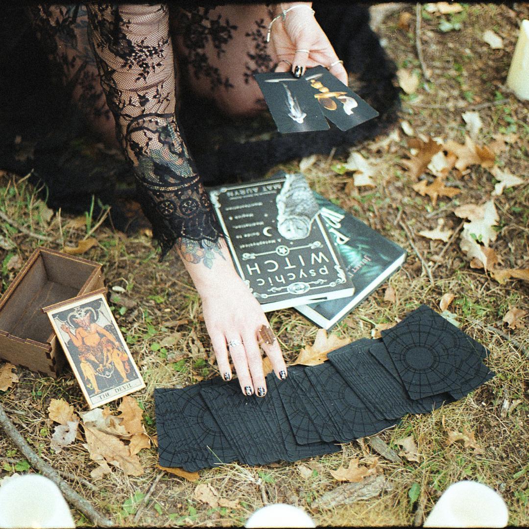 tarot cards spread on forest floor with witch book and hands reaching for cards